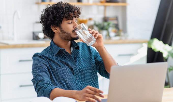 Ein Mann trinkt ein Glas Wasser vor seinem Laptop