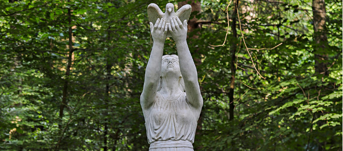 Eine Steinstatue, die eine Taube in den Händen hält, die sie in den Himmel streckt.