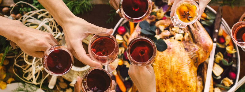 Personen stoßen mit Weingläsern an einem weihnachtlich und festlich gedeckten Tisch an.