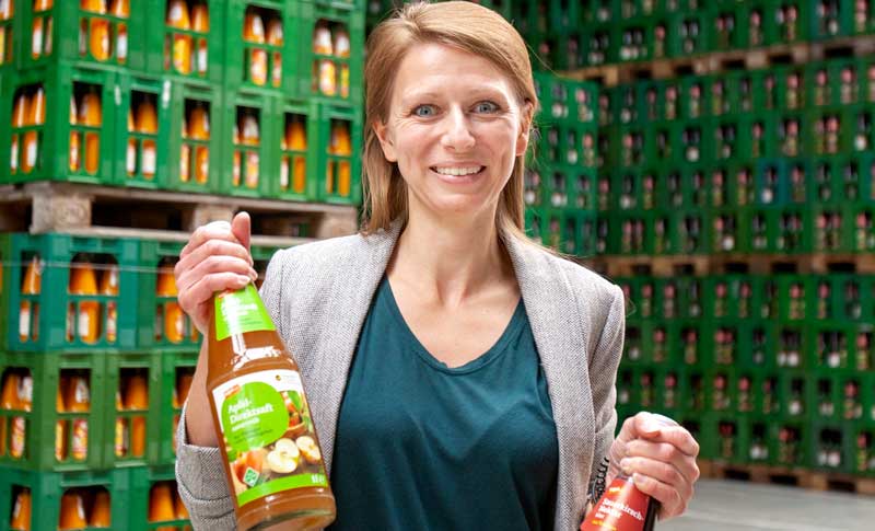Das Bild zeigt die Ökotrophologin Jessica Liebetrau im Getränkelager mit einer Flasche Apfelsaft in der Hand.