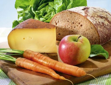 Regionale Lebensmittel auf einem Holzbrett, Brot, Möhren, Käse, Apfel und Salat.
