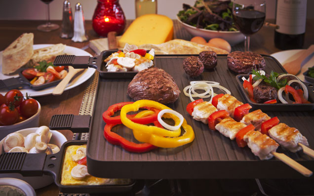 Raclettegerät mit vielen Zutaten wie Fleisch, Gemüse, Käse und Dips