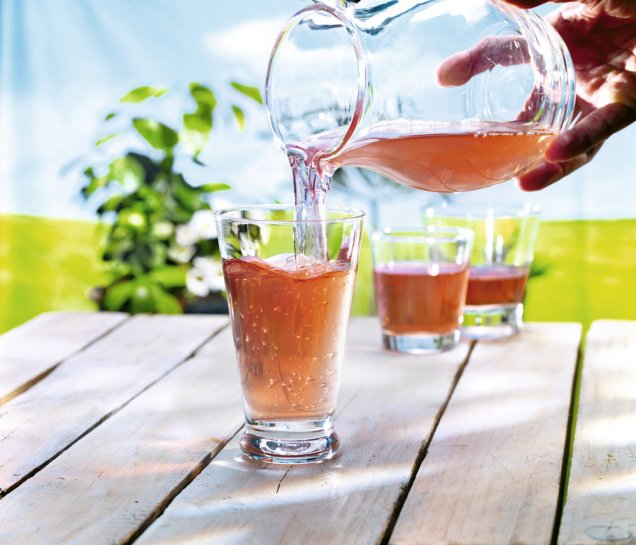 Rhabarber-Nektar mit Wasser wird aus einer Glaskaraffe in ein Glas eingeschenkt.